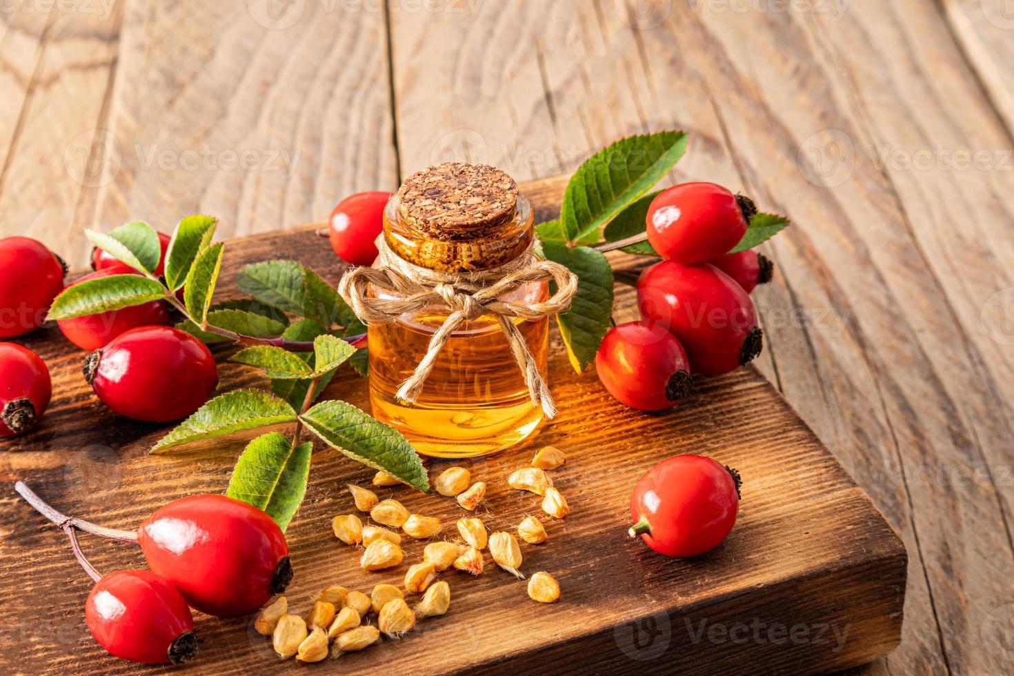 una botella de vidrio con un corcho con aceite de semilla de rosa mosqueta natural sobre una tabla de madera entre las frutas y semillas. vista frontal. foto