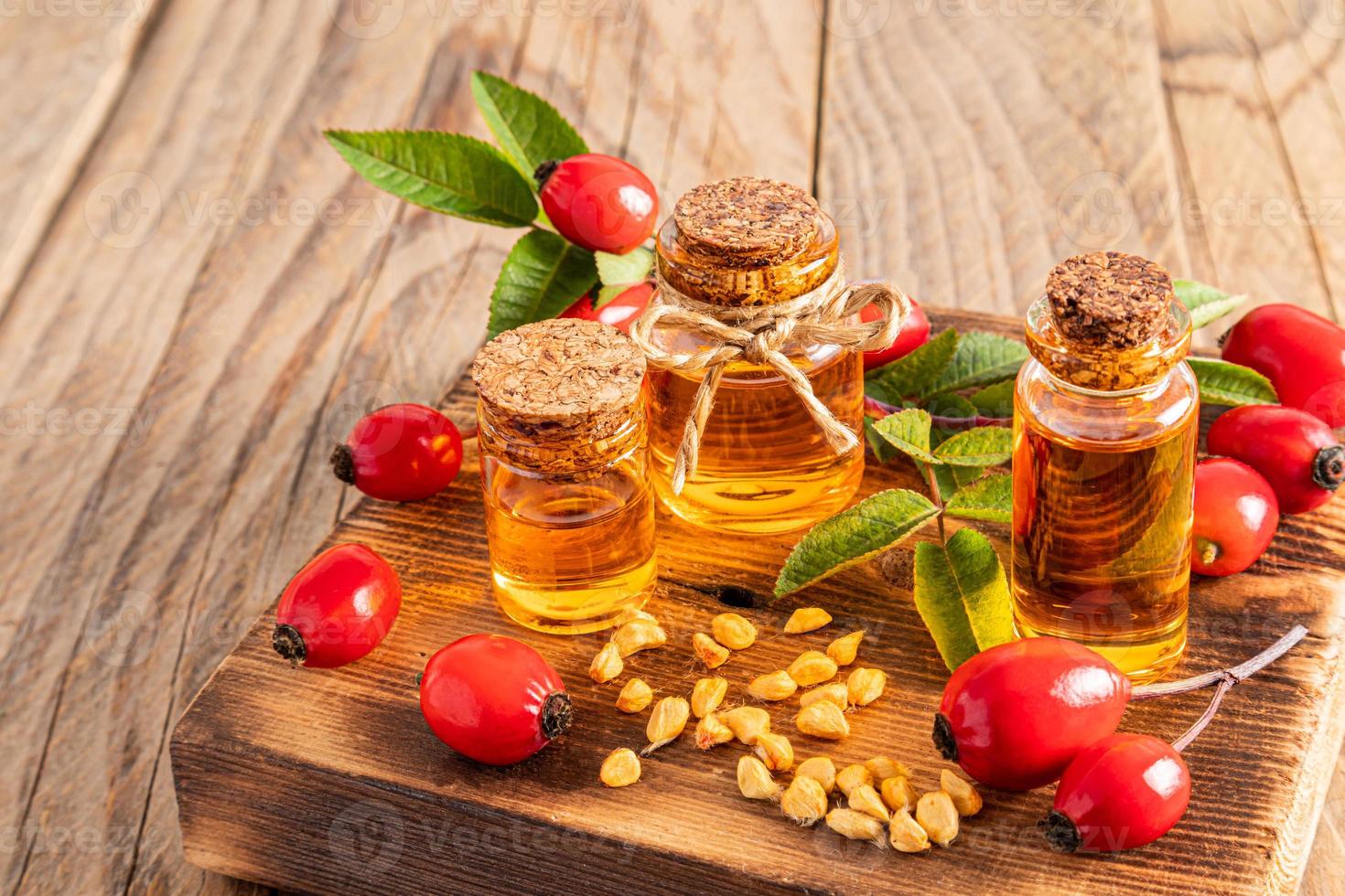 a set of glass bottles with a cork with organic rosehip seed oil on a wooden podium with radish fruits of the plant. front view. Vitamins. photo