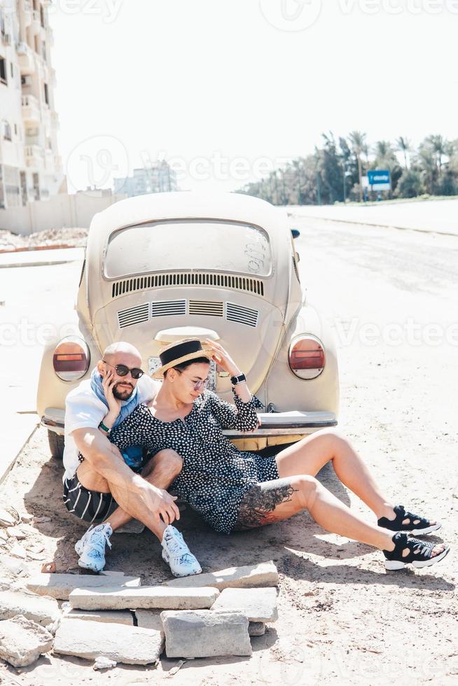 Couple sitting on the asphalt behind the car photo