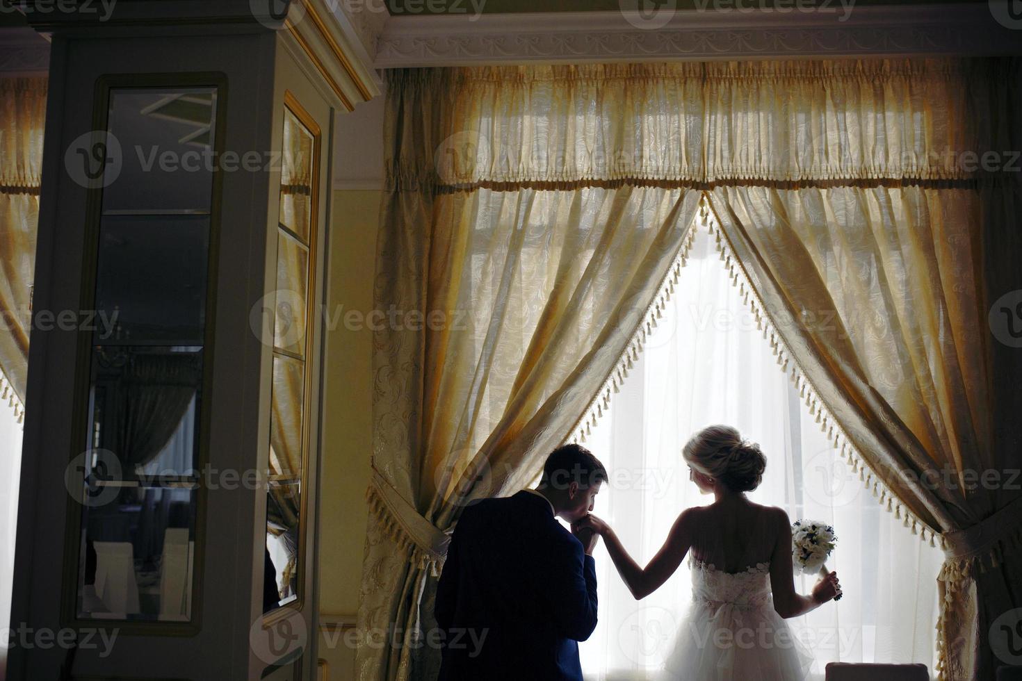 bride and groom standing in front of window photo