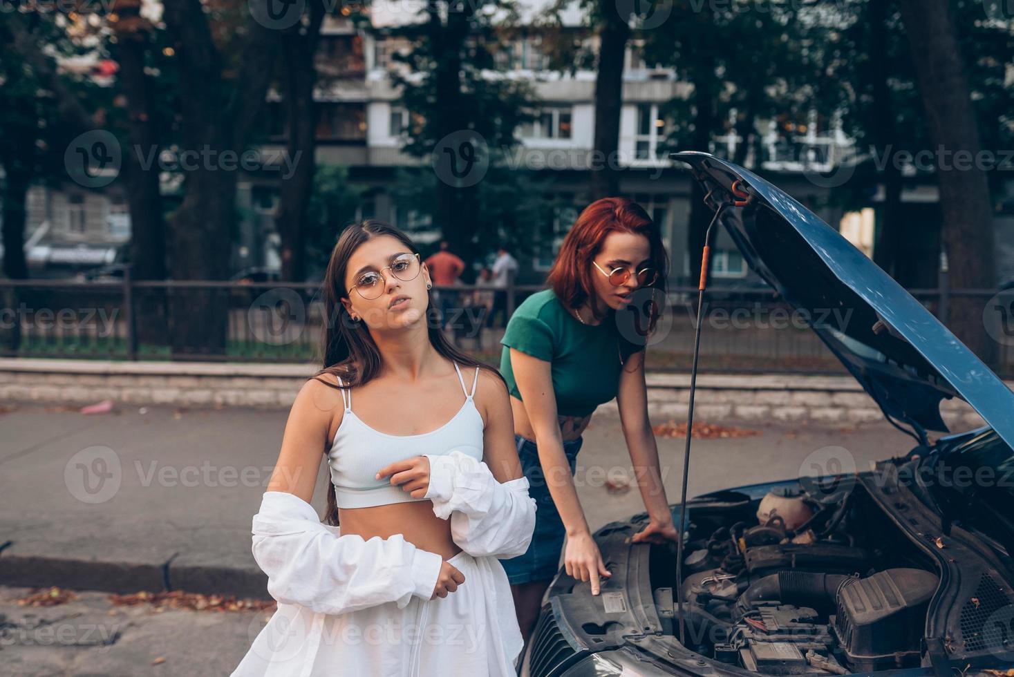 Two women with broken car on the road. Open hood photo