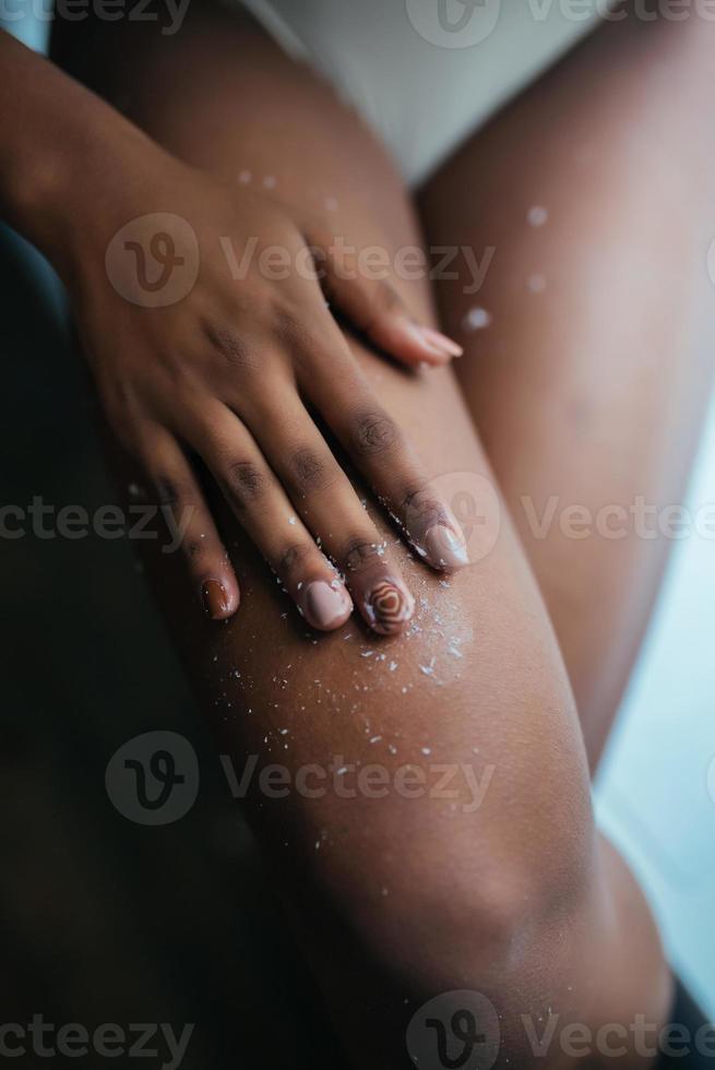 hermosa joven afroamericana aplicando exfoliante en las piernas foto