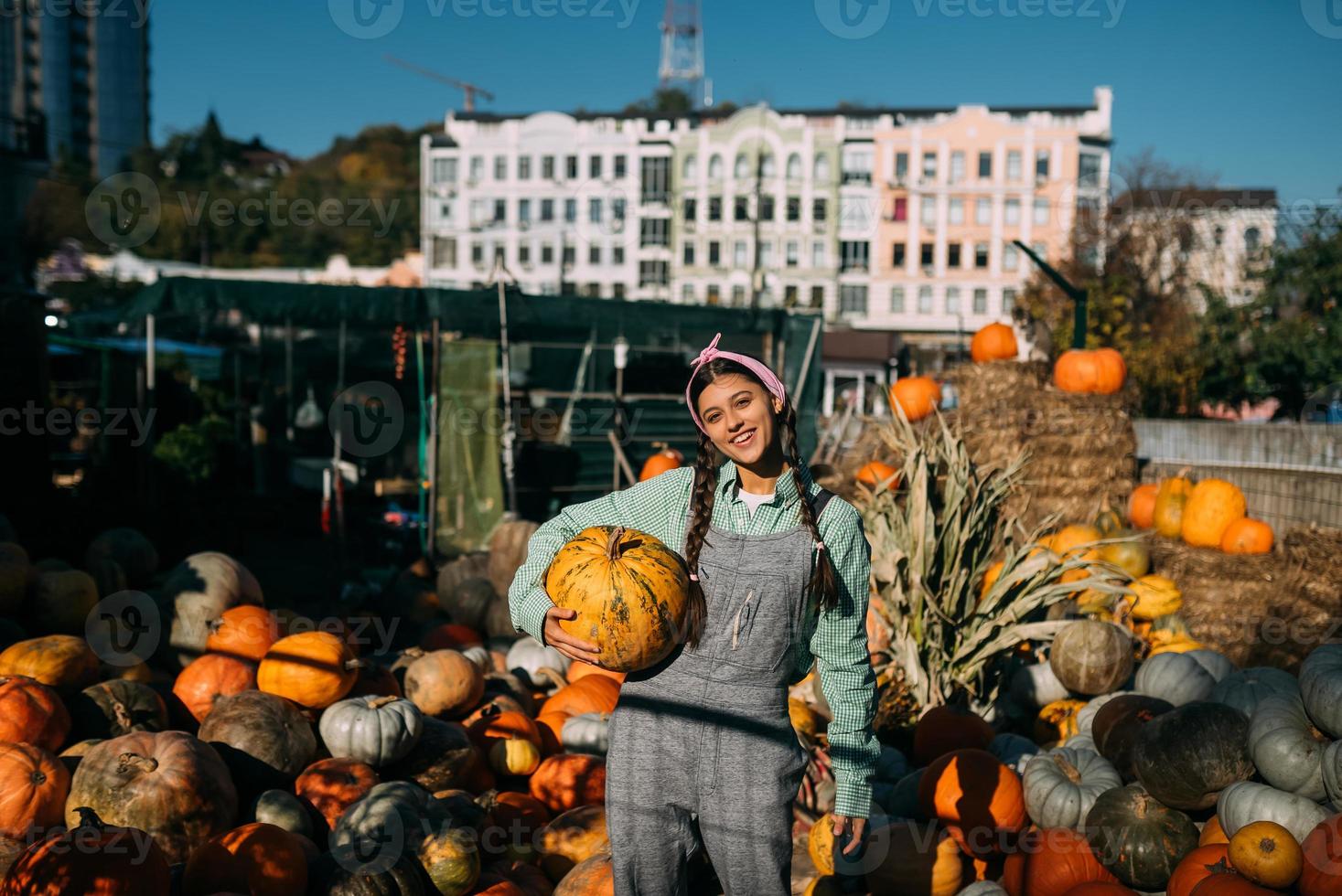 Happy farmer woman in a denim jumpsuit holds ripe pumpkin photo