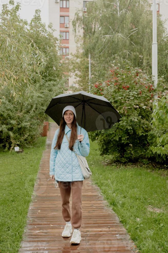 a girl in a blue jacket walks in the park along a wooden path with an umbrella photo