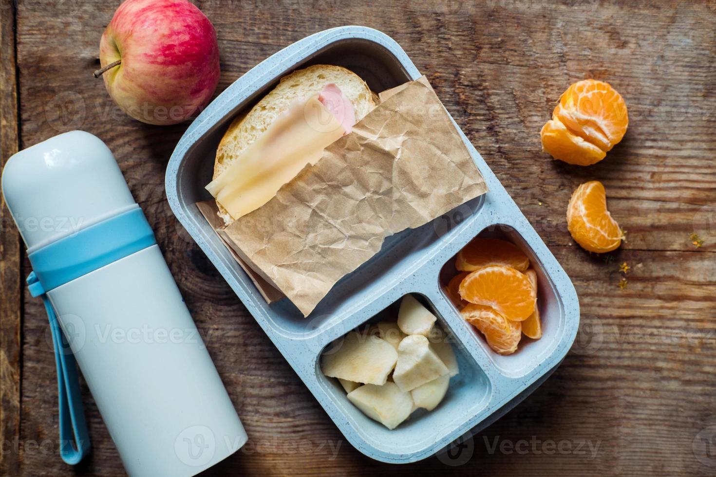 schoolboy lunch box with thermos on wooden background.apple,tangerine,sandwich in lunchbox and water bottle photo