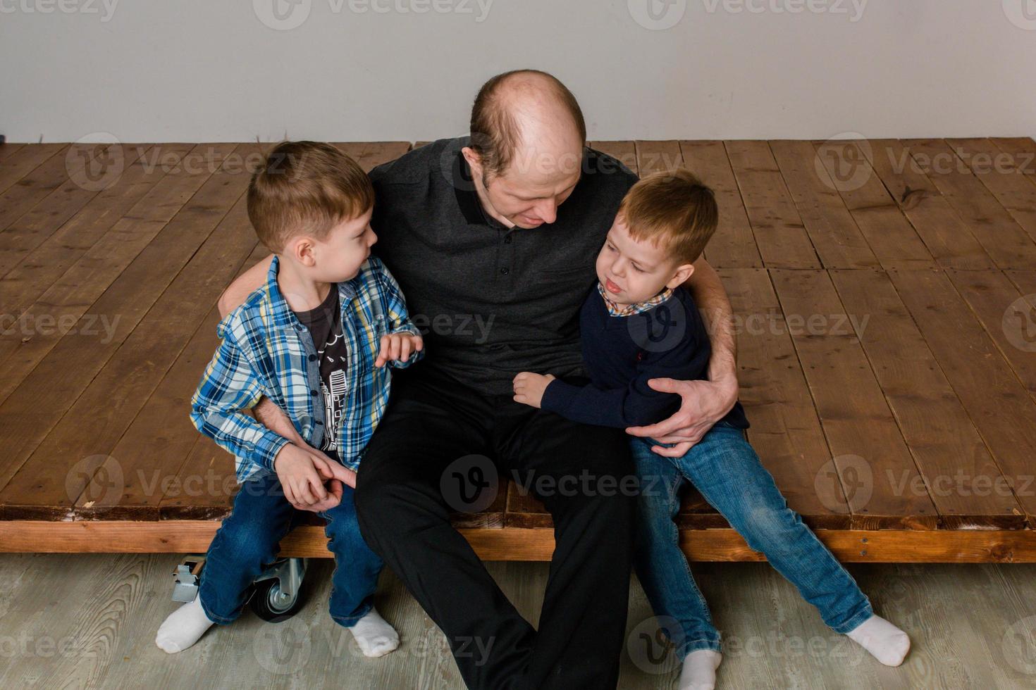 dad sits with two sons on the floor and hugs them. Warm relationship dad and sons photo
