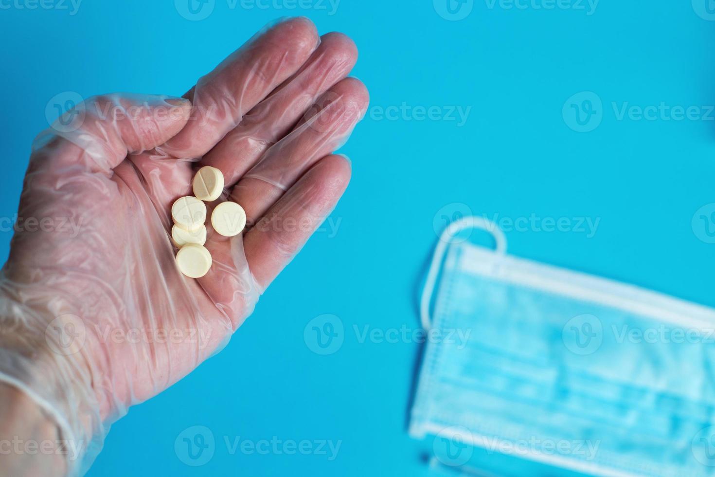 la máscara médica y las tabletas se cierran sobre el fondo azul. la mano sostiene la píldora. coronavirus, concepto de enfermedad respiratoria gripal foto