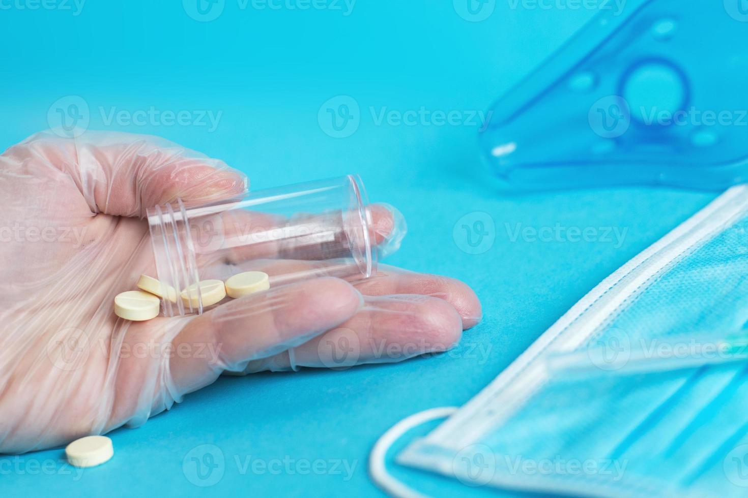 máscara médica, jeringa, máscara para inhalación y tabletas se cierran sobre el fondo azul. mano sostiene pastillas. coronavirus, gripe foto