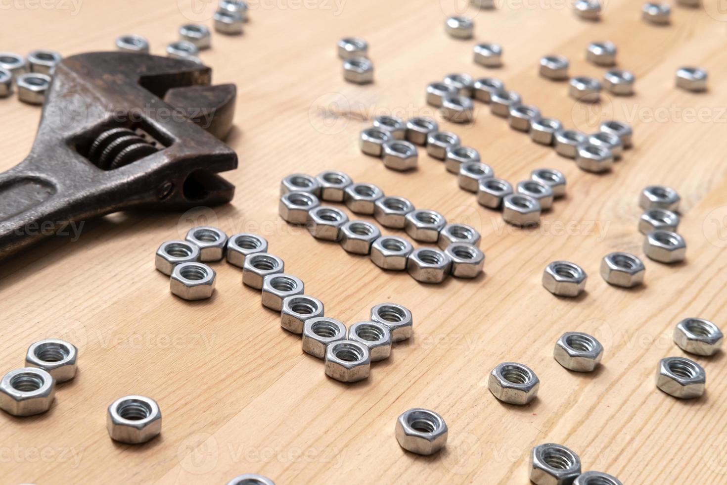 Number 2022 is lined with metal nuts on a wooden table next to a large, old wrench photo