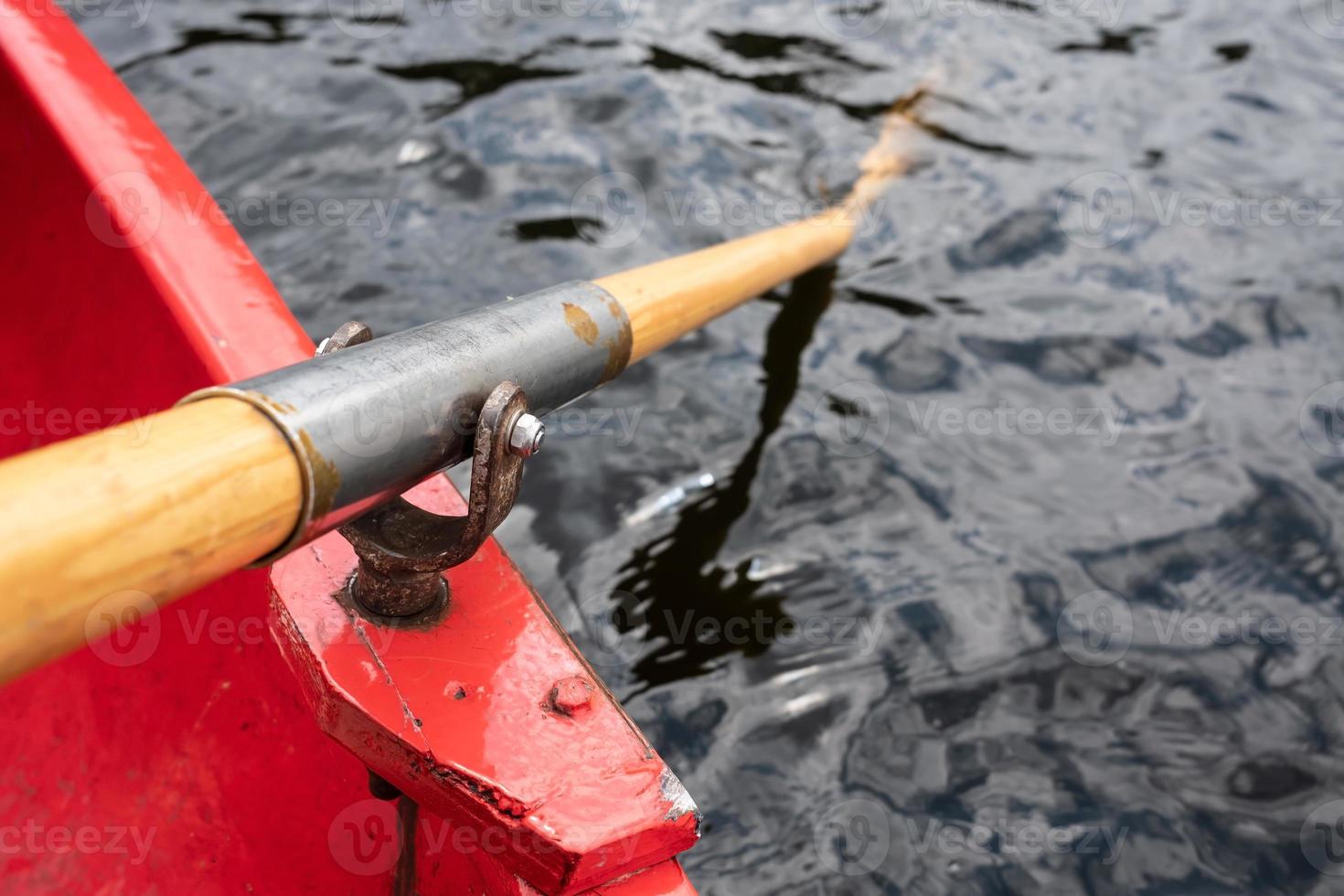 Oar is held on an oarlock attached to a red boat, against the background of water. photo