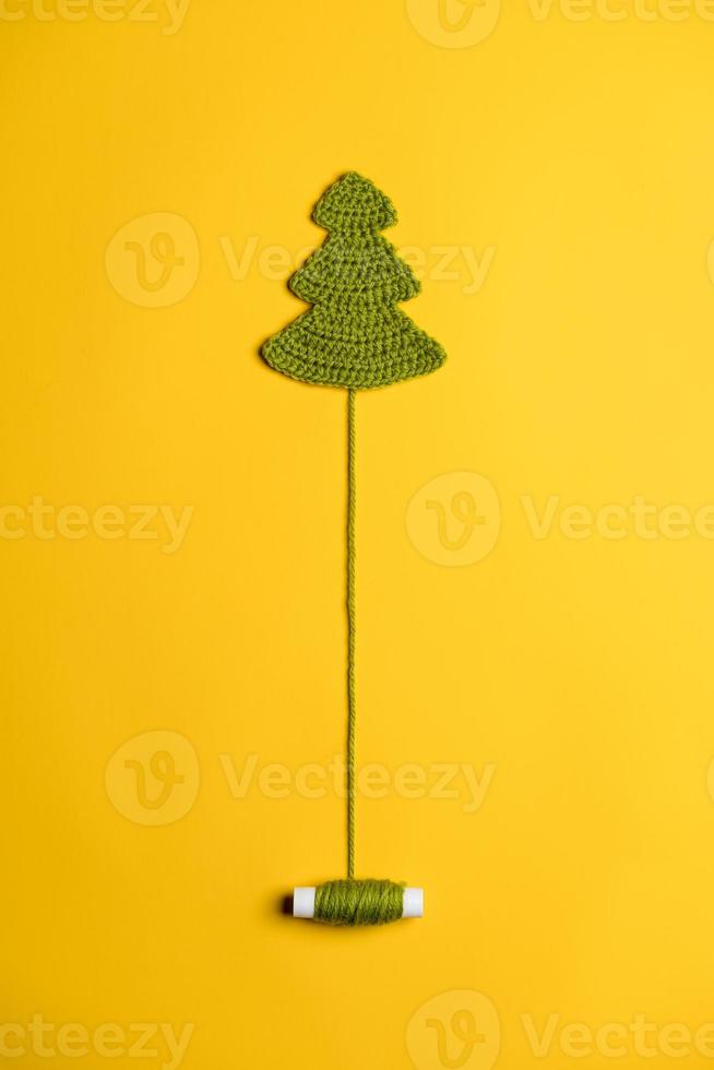Knitted Christmas tree - a symbol of the New Year, with an unwound spool of thread like a trunk, on a yellow background. Top view. photo