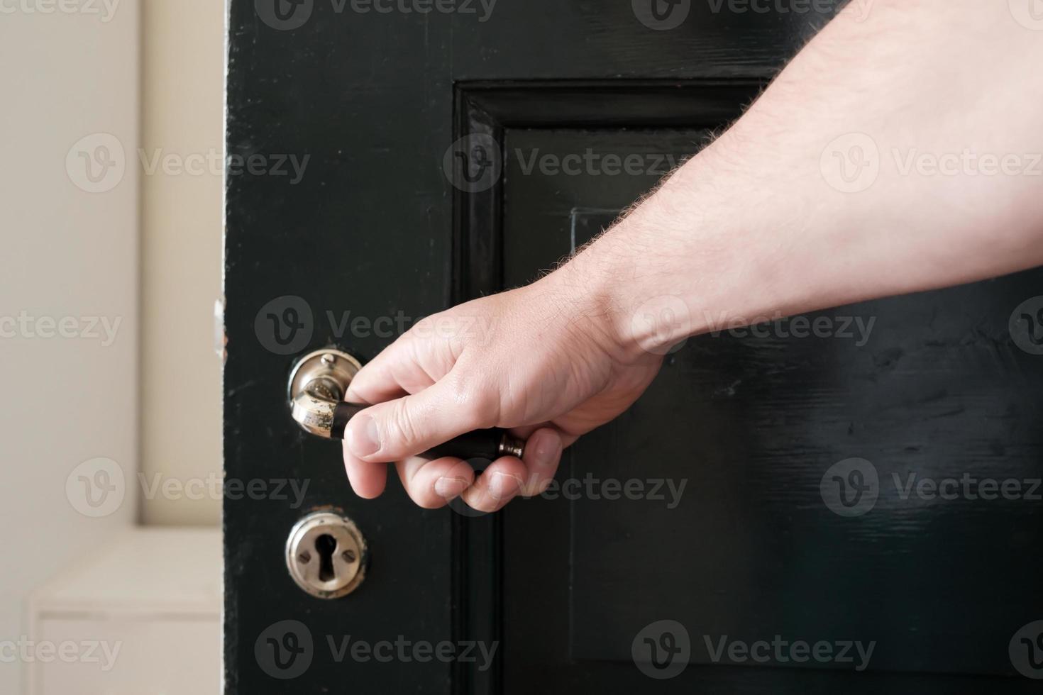 la mano masculina quiere cerrar una puerta de madera negra, sujetando un mango de metal, contra el fondo de una pared blanca. foto