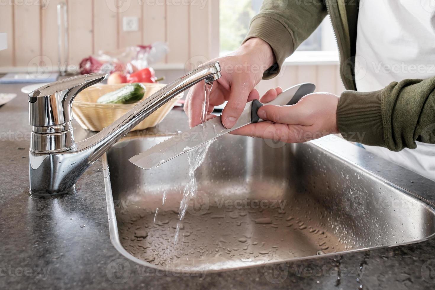 Male hands wash the knife under running water, in the sink, in the kitchen. photo