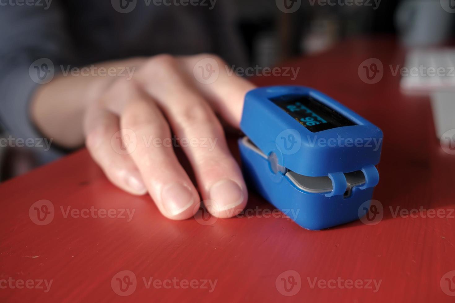 Woman uses a pulse oximeter to measure pulse rate and blood oxygen levels on a red table in an apartment. photo