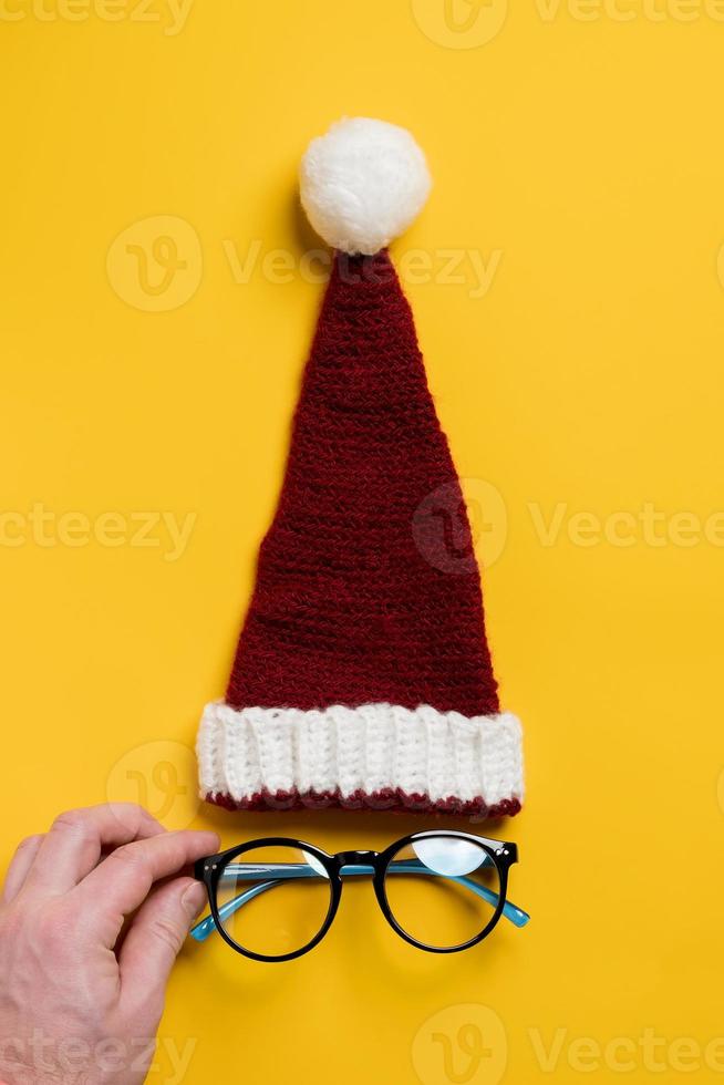 Red and white knitted hat of Santa Claus and the glasses under it, which are straightened by the hand, looks like a face. photo