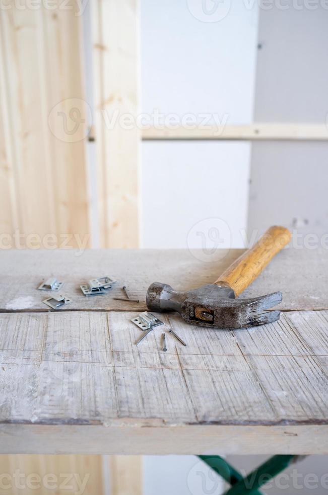 Hammer and nails lie on the scaffolding, against the background of a wall made of wooden slats. Work process. Home renovation. photo