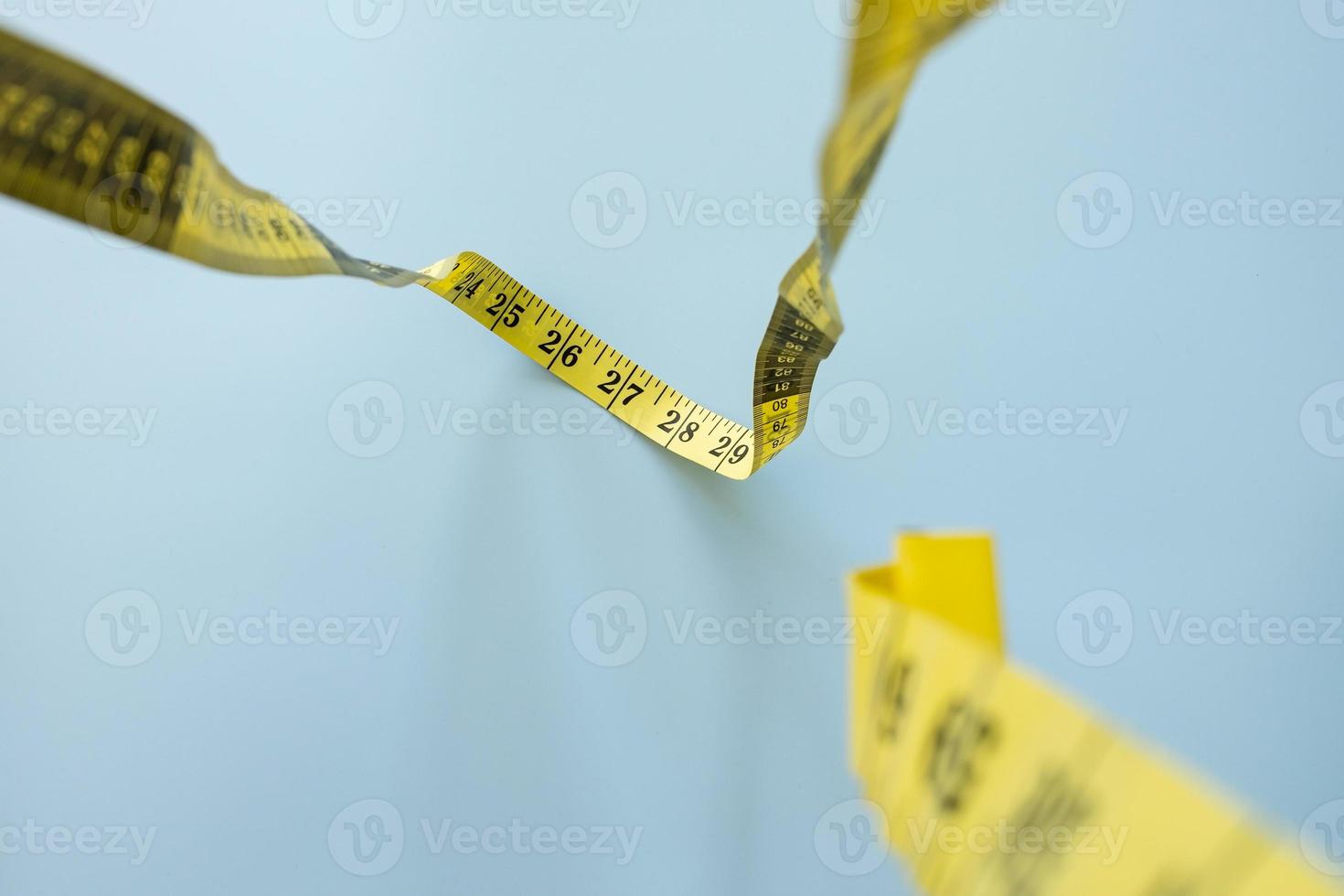Centimeter tape hangs down on a blue background, top view. Tailor meter for sewing. Concept of weight loss, a tape measure for measuring the waist. photo