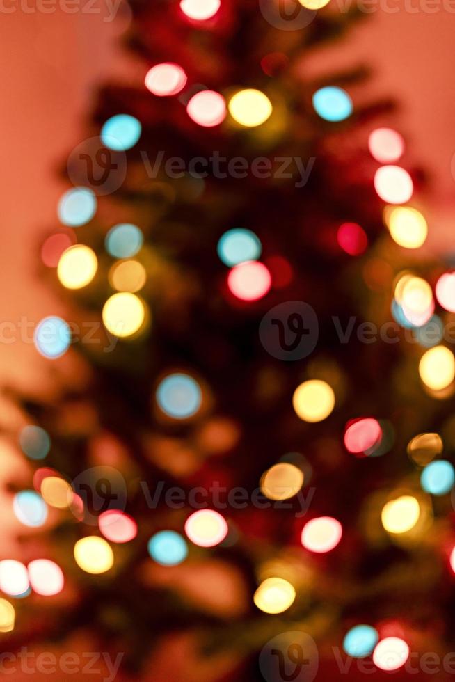 merry christmas background with christmas tree and blurry lights garland on red backdrop in defocus photo