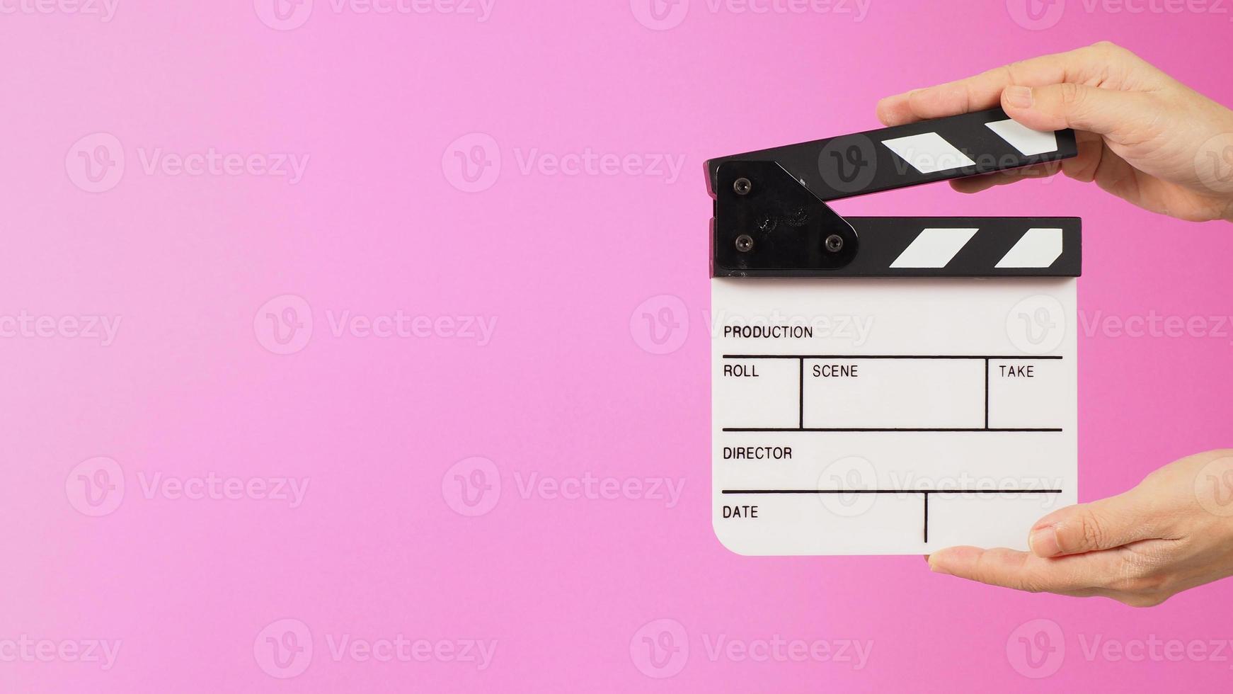 Two hands are holding a small white clapper board or movie slate on pink background. Side view photo