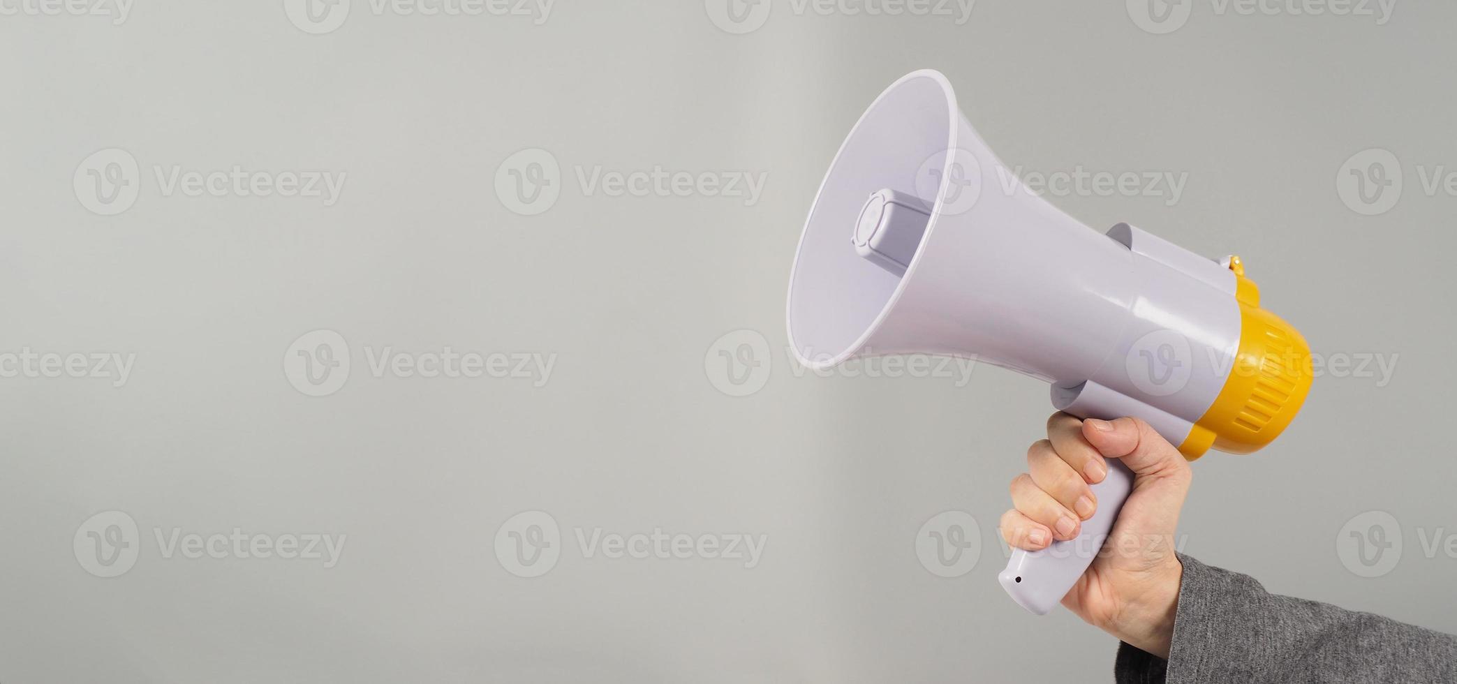 A hand is holding megaphone and  wearing a dark grey T-shirt on grey background. photo