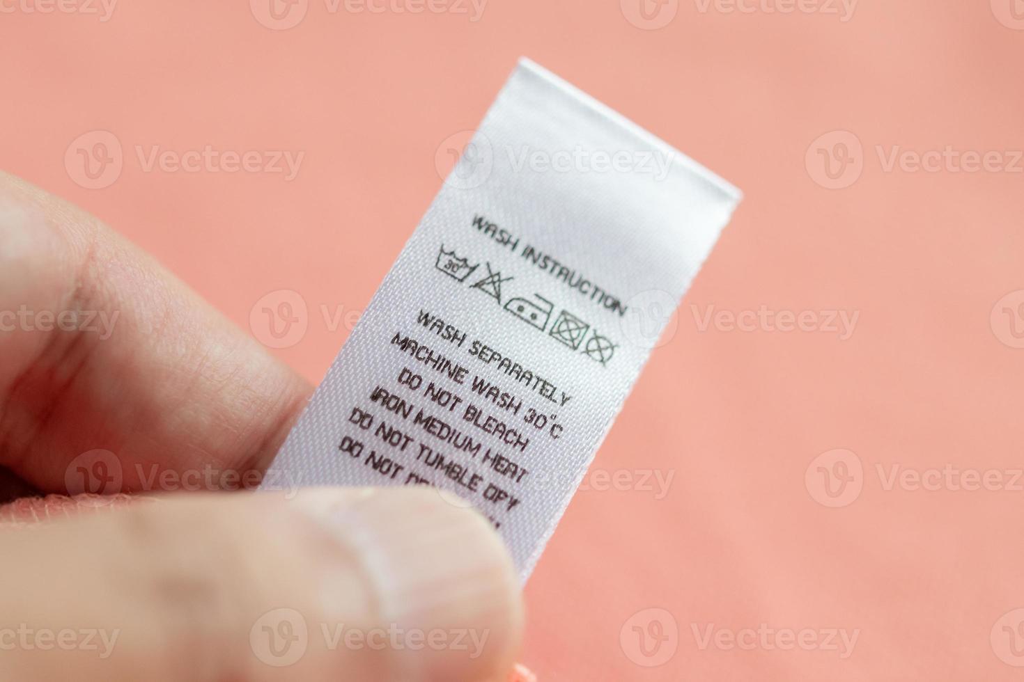Hand hold and reading at white laundry care washing instructions clothes label on pink shirt photo