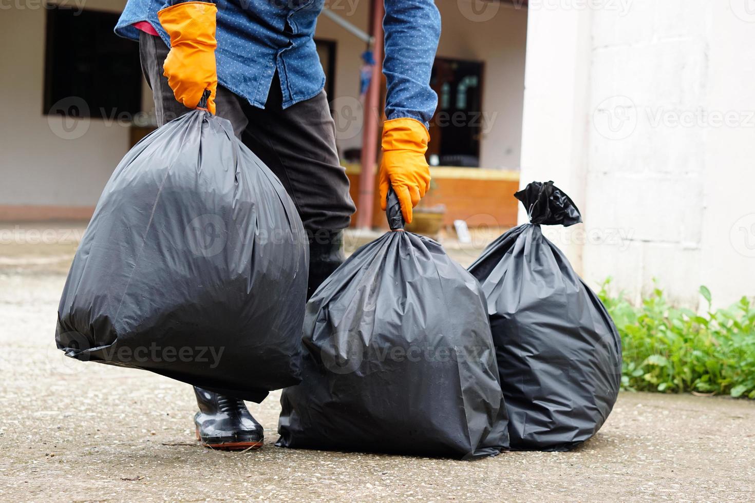 Closeup man holds black plastic bag that contains garbage inside, stand in front of house. Concept , Waste management. Environment problems. Daily chores. Throw away rubbish . photo