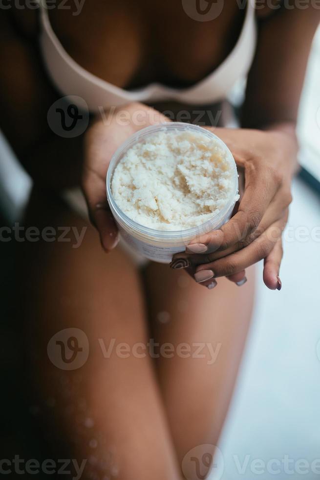 Black-skinned model dressed in underwear holds a jar with a scrub photo