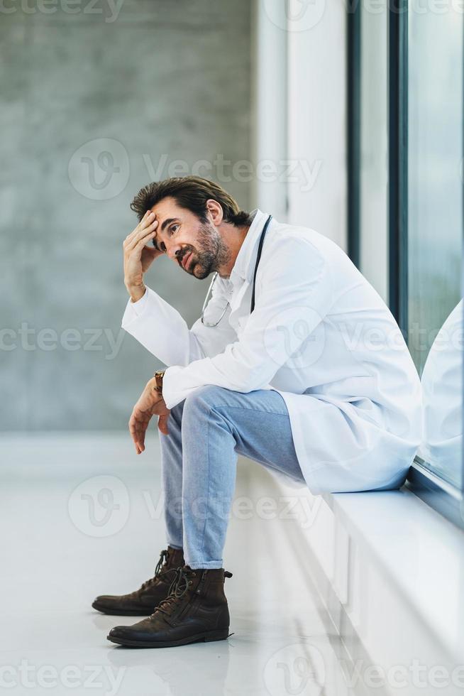 un médico pensativo que parece preocupado durante un descanso rápido en un pasillo vacío del hospital foto