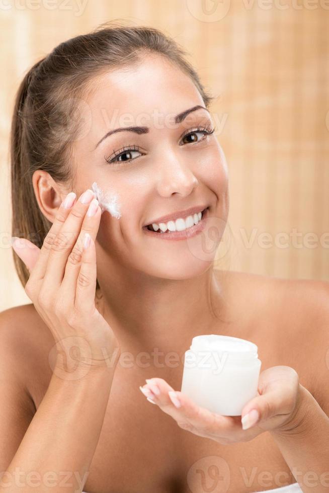 mujer joven poniéndose crema facial foto