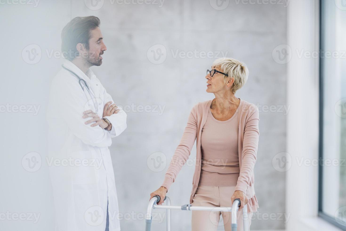 Senior Woman Using A Mobility Walker And Talking With Doctor In The Hospital Hallway photo