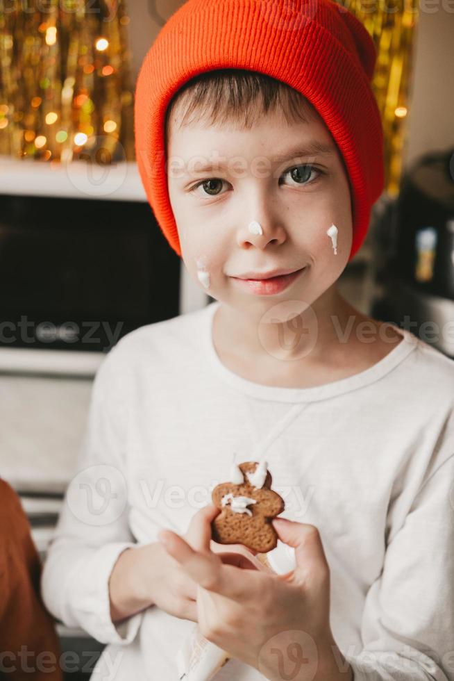 Boy decorate Christmas cookies with white icing. Children decorate a gingerbread man on a wooden background. Christmas sweets with cocoa and marshmallows for children. photo
