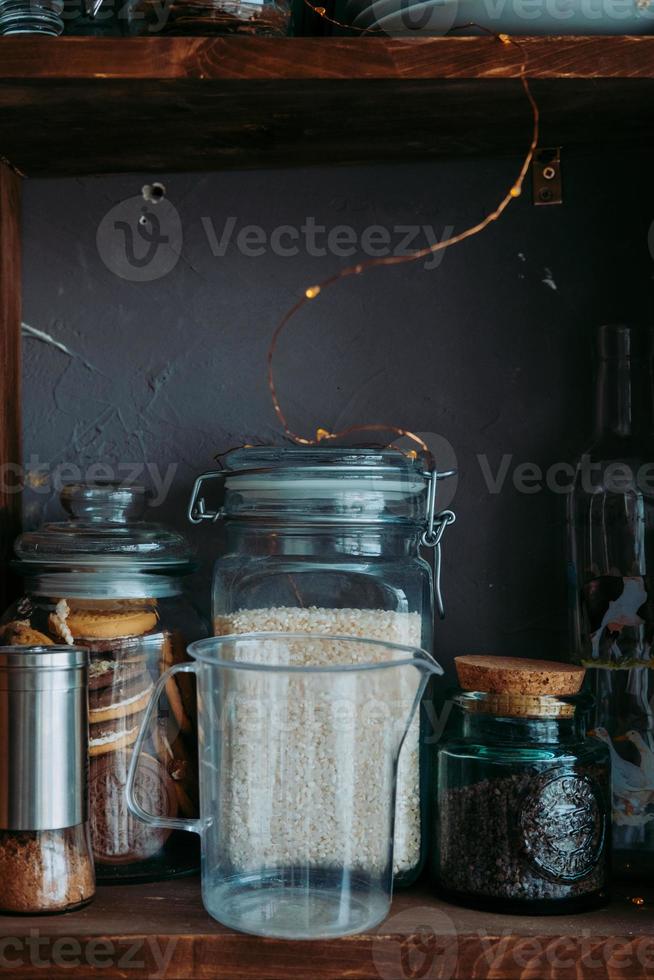 shelf with spices in the kitchen. Grocery shelf in glass jars. Measuring glass in the kitchen. Interior elements with a garland photo