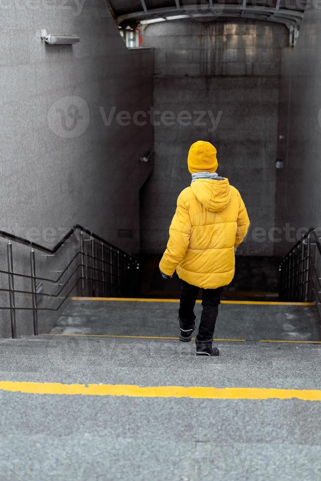 niño en la escalera mecánica del metro. un niño sonriente baja por las escaleras mecánicas del metro. el concepto de autosuficiencia del niño foto