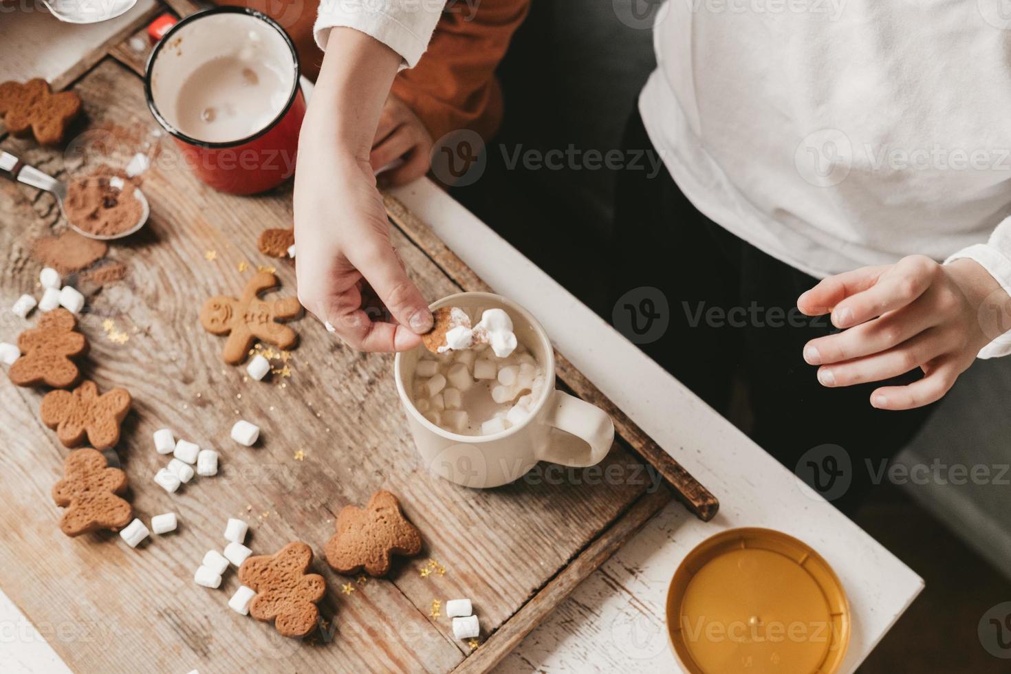 Children drink cocoa with marshmallows and christmas gingerbread man on a wooden background. Christmas sweets with cocoa and marshmallows for children. Winter vacation at home photo
