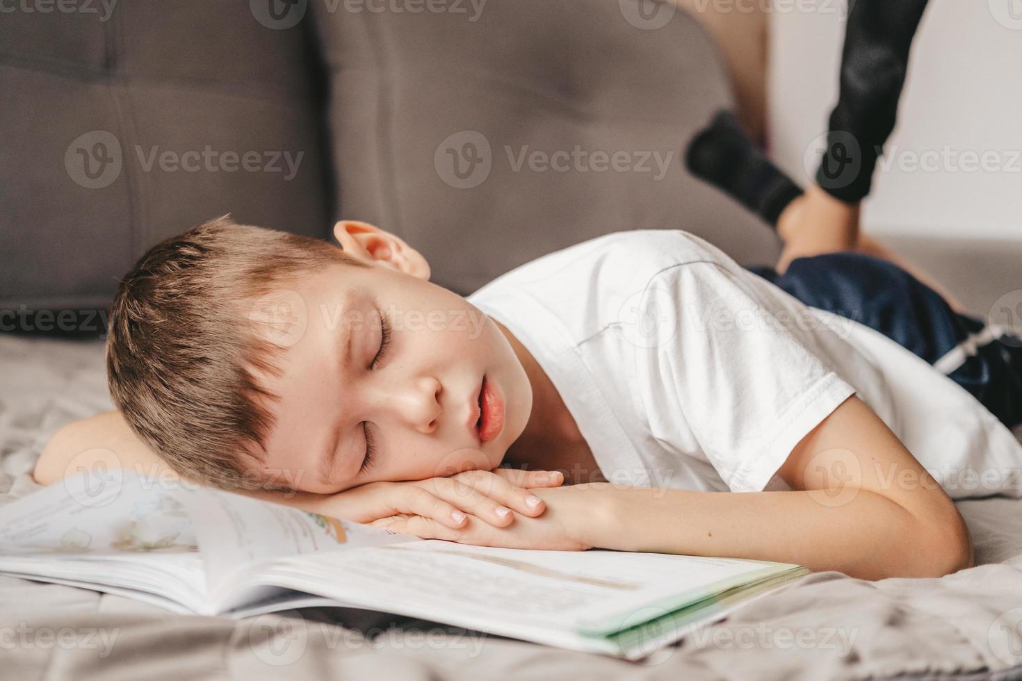 portrait of a boy who fell asleep during homework lying on the couch. Teenager over a notebook, on the bed. Homeschooling a 9 year old boy. Difficult study photo