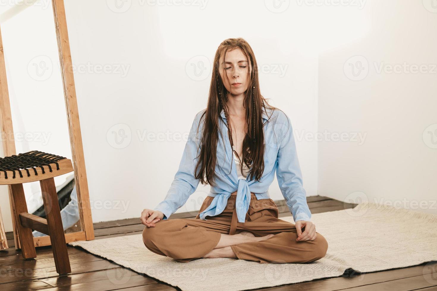 girl with long and dark hair sitting lotus pose meditating on floor light room interior. Yoga practice photo