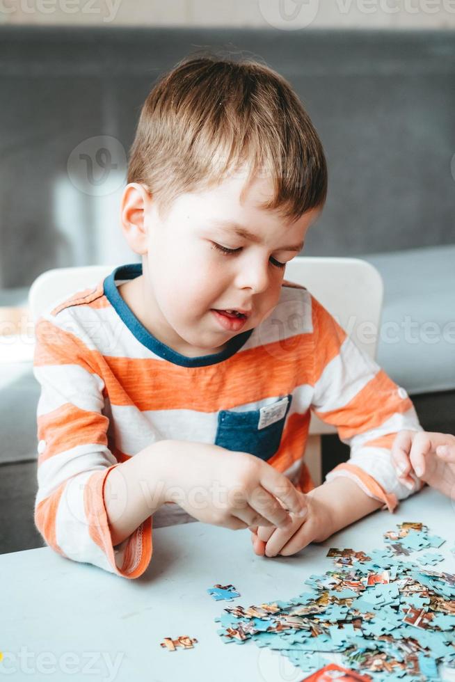 boy in an orange T-shirt collects a puzzle on the table. time without gadgets. board games for children. The boy develops fine motor skills and brain photo