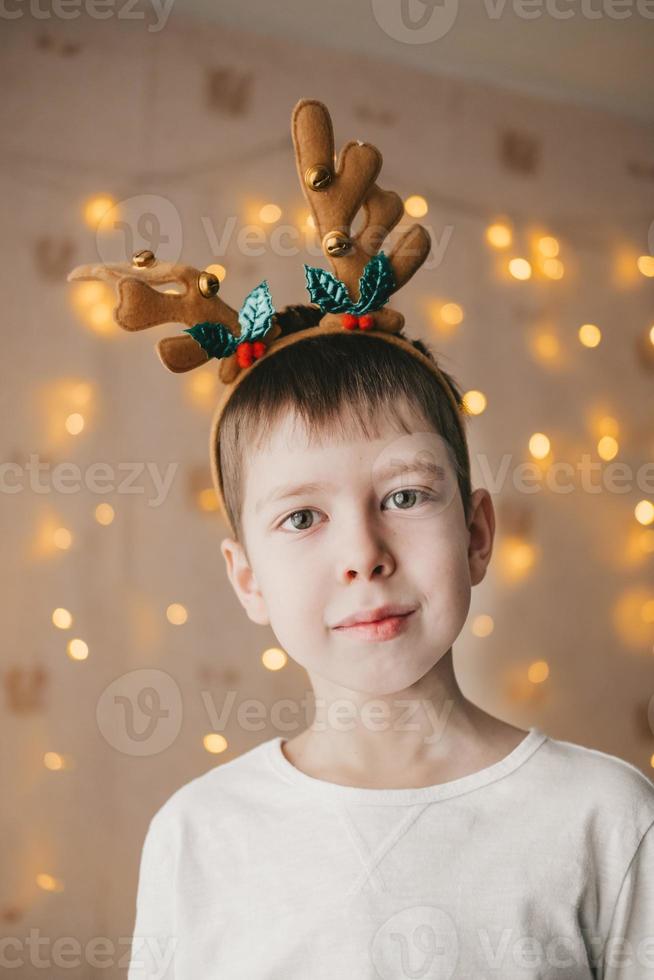 retrato de un niño con cuernos navideños de reno en el fondo de una guirnalda naranja. preparándose para la fiesta de navidad. disfraces de año nuevo de niños foto