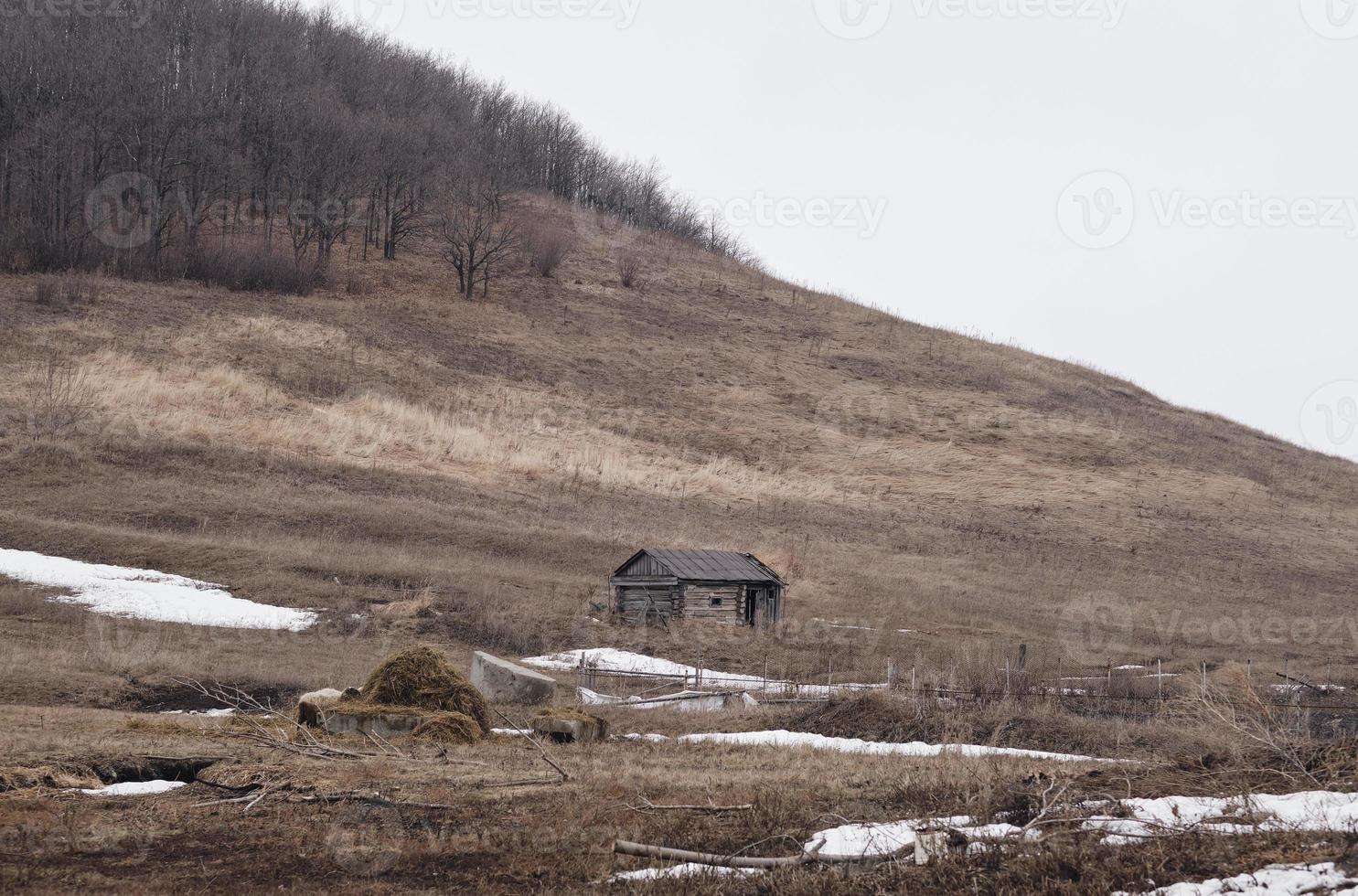 Old abandoned wooden hut on background of green hills. Gloomy weather. Grey clouds photo