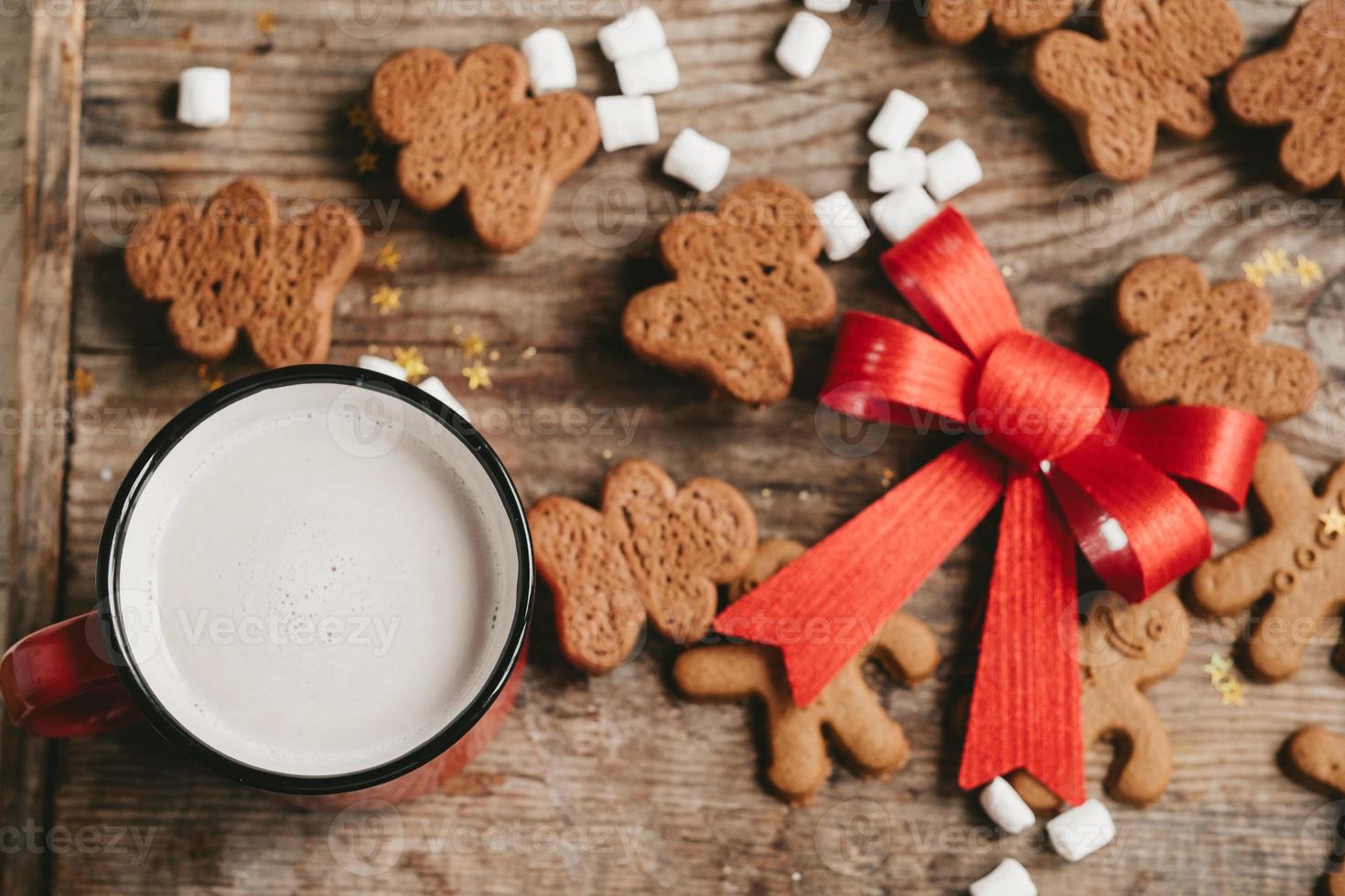 gingerbread man, cocoa and cookies with a big red bow on a wooden background, top view. Various christmas sweets with a cup of cocoa on the table photo