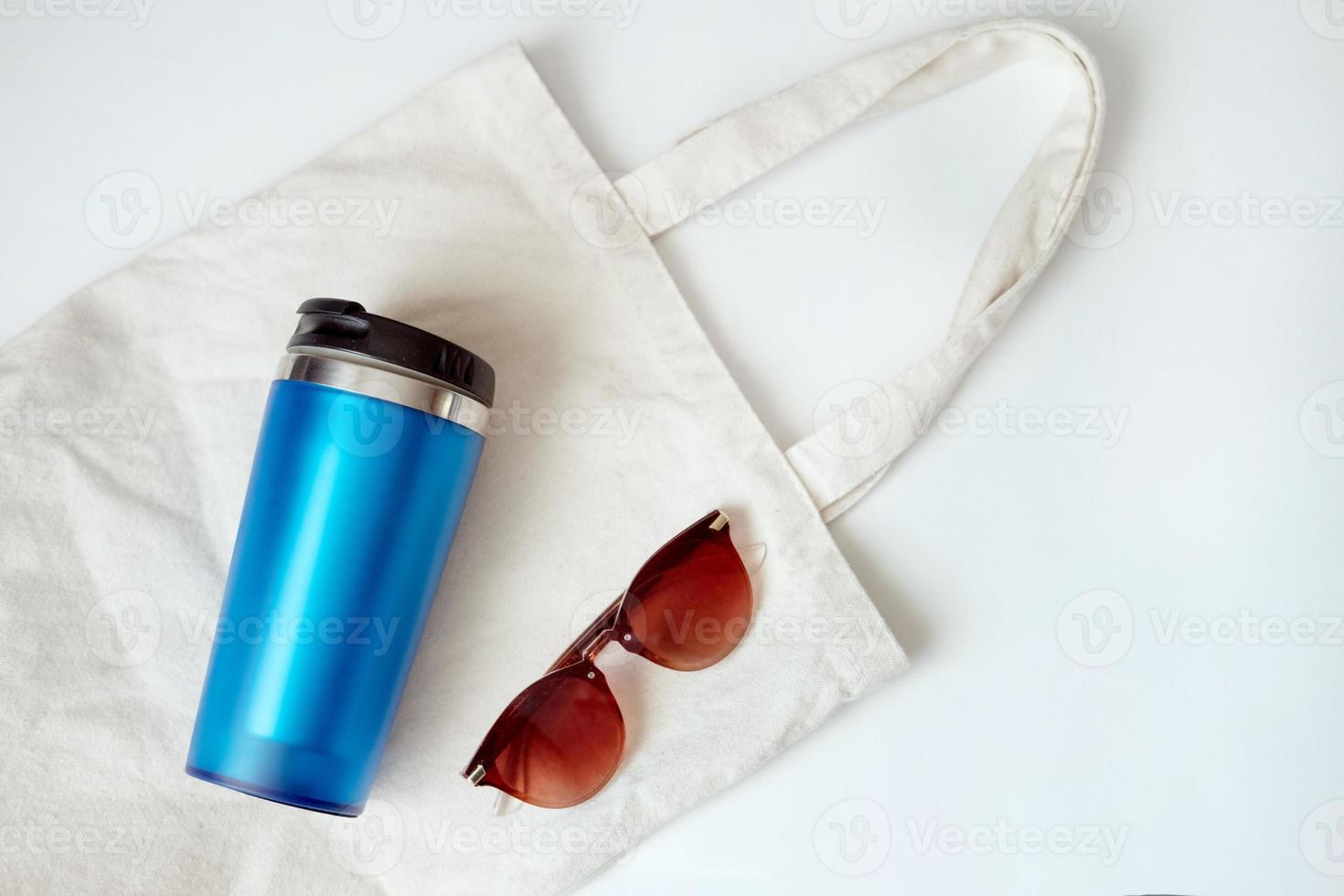 bolsa de lona, termo azul y gafas de sol. listo para caminar en el parque. conjunto de playa. preparación de vacaciones. estilo ecológico foto