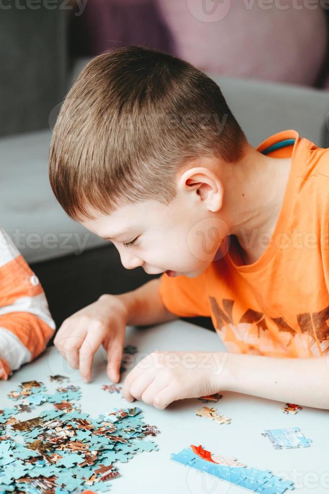 boy in an orange T-shirt collects a puzzle on the table. time without gadgets. board games for children. The boy develops fine motor skills and brain photo