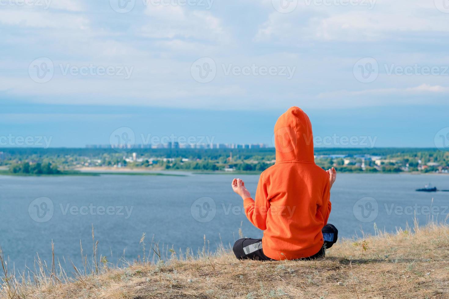 boy meditates on the hillside against the background of the sea. Beautiful seascape with a meditating boy from the back. Mental health from childhood. Harmony with nature. photo
