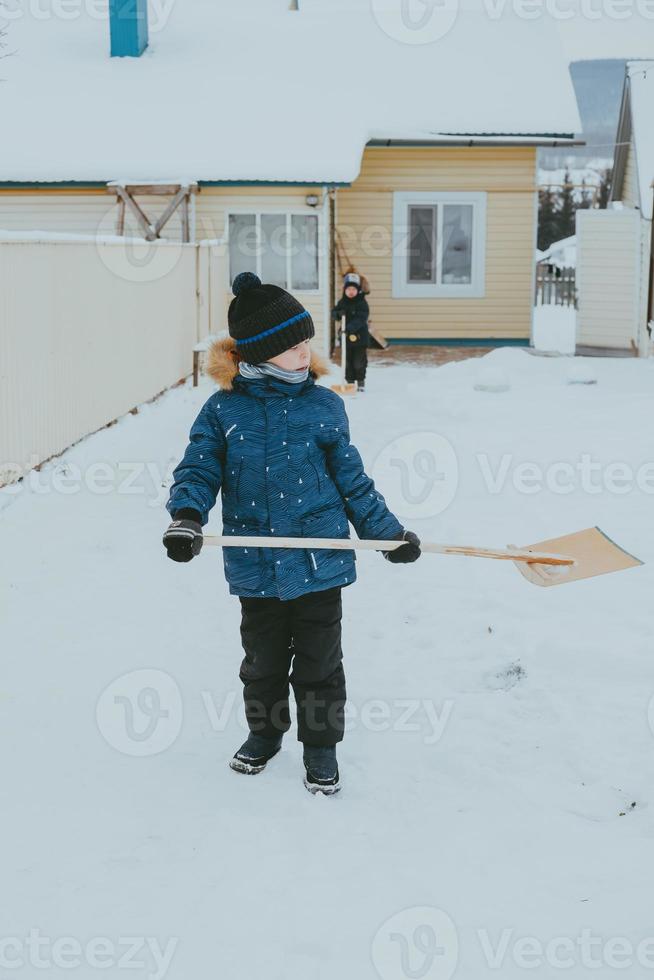 boy cleans snow with a shovel on the street. A boy clears the road from snow in winter. Hardworking child. A boy living in the village cleans the snow. photo