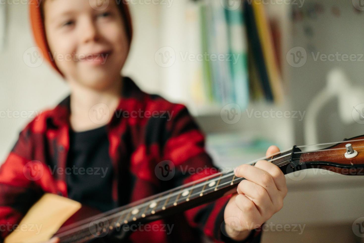 boy in a red hat and a plaid shirt plays the balalaika. Close-up hands playoul. ing the guitar.Music lessons at home. Hobby for the soul. photo