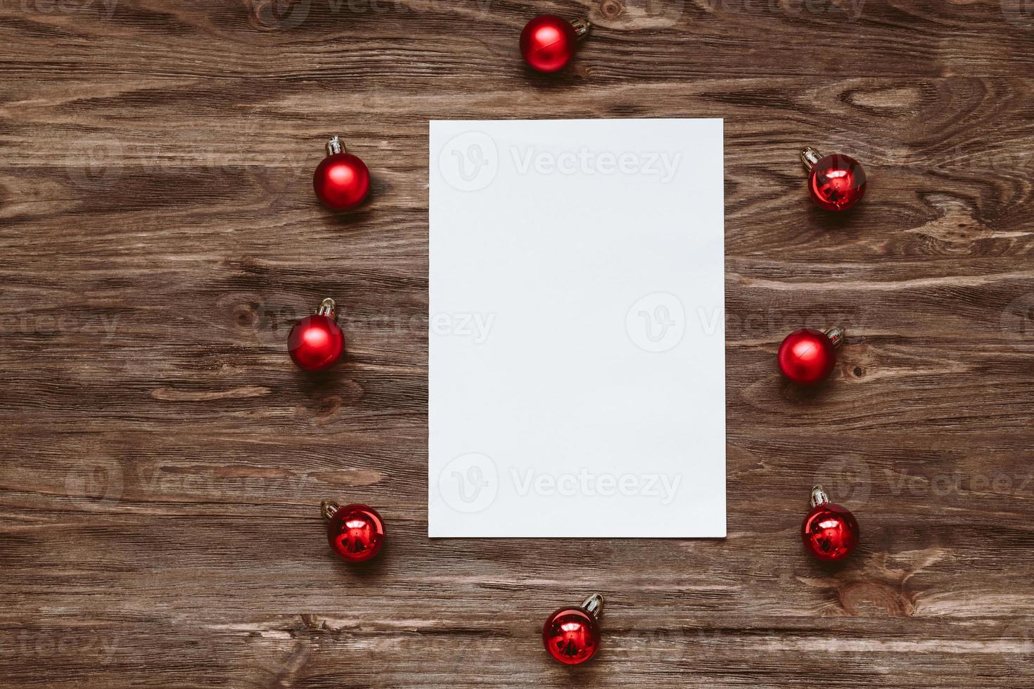 A blank sheet of paper and and red Christmas balls on a wooden background. Top view, flat lay photo