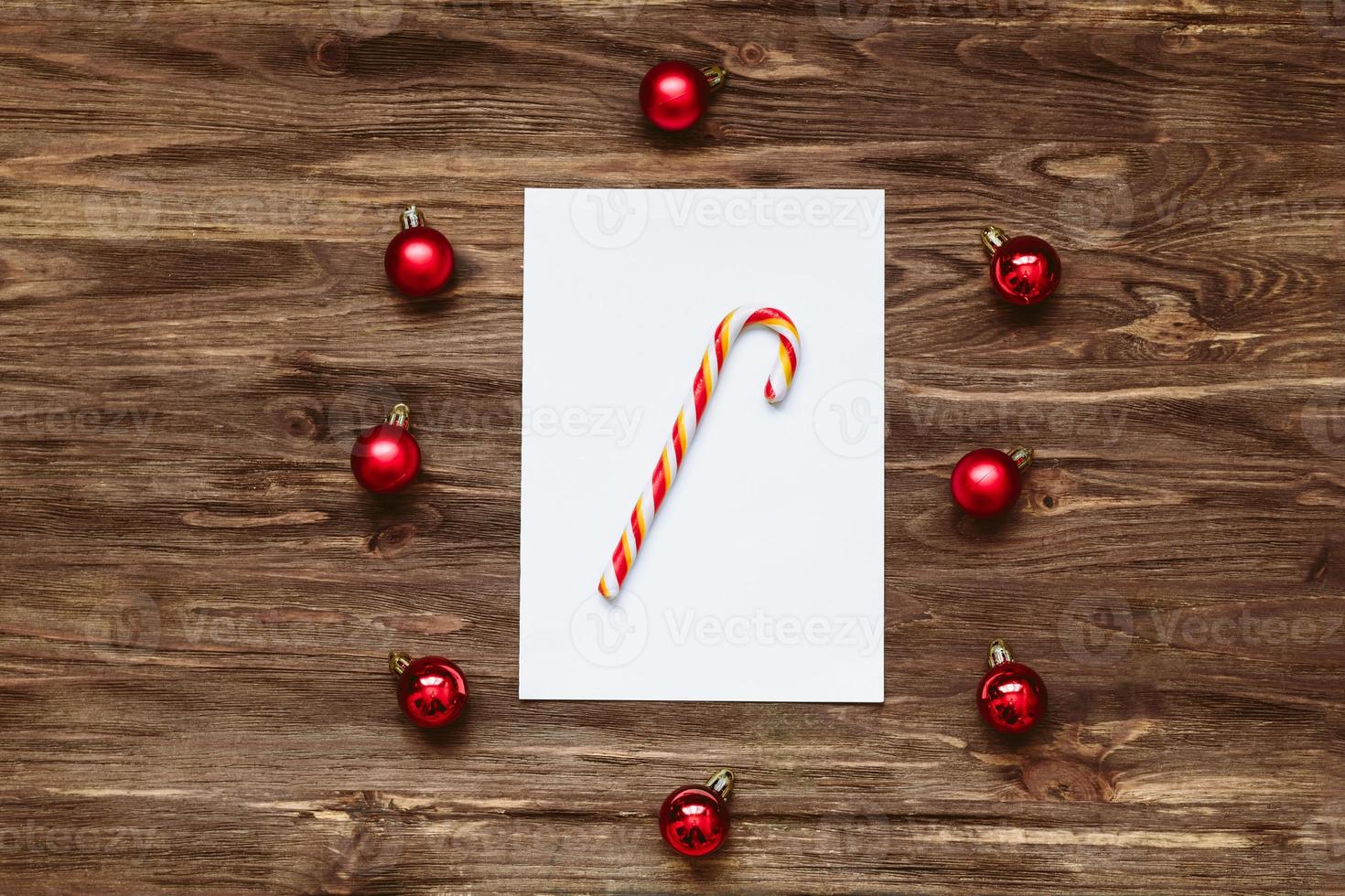 Striped lollipop on a Blank sheet of paper and and red Christmas balls on a wooden background. Top view, flat lay photo