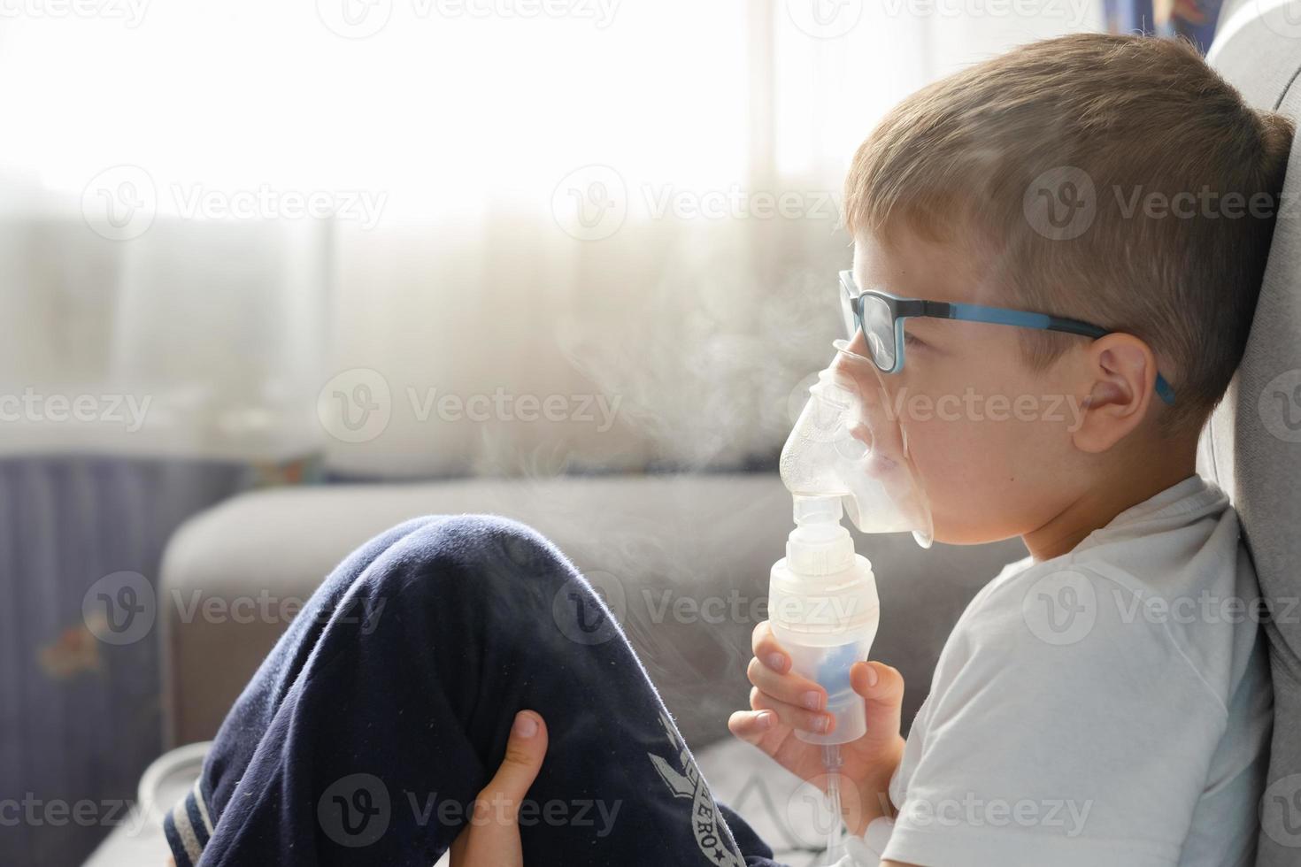 un niño pequeño se sienta con una máscara de inhalación durante la tos y la bronquitis foto