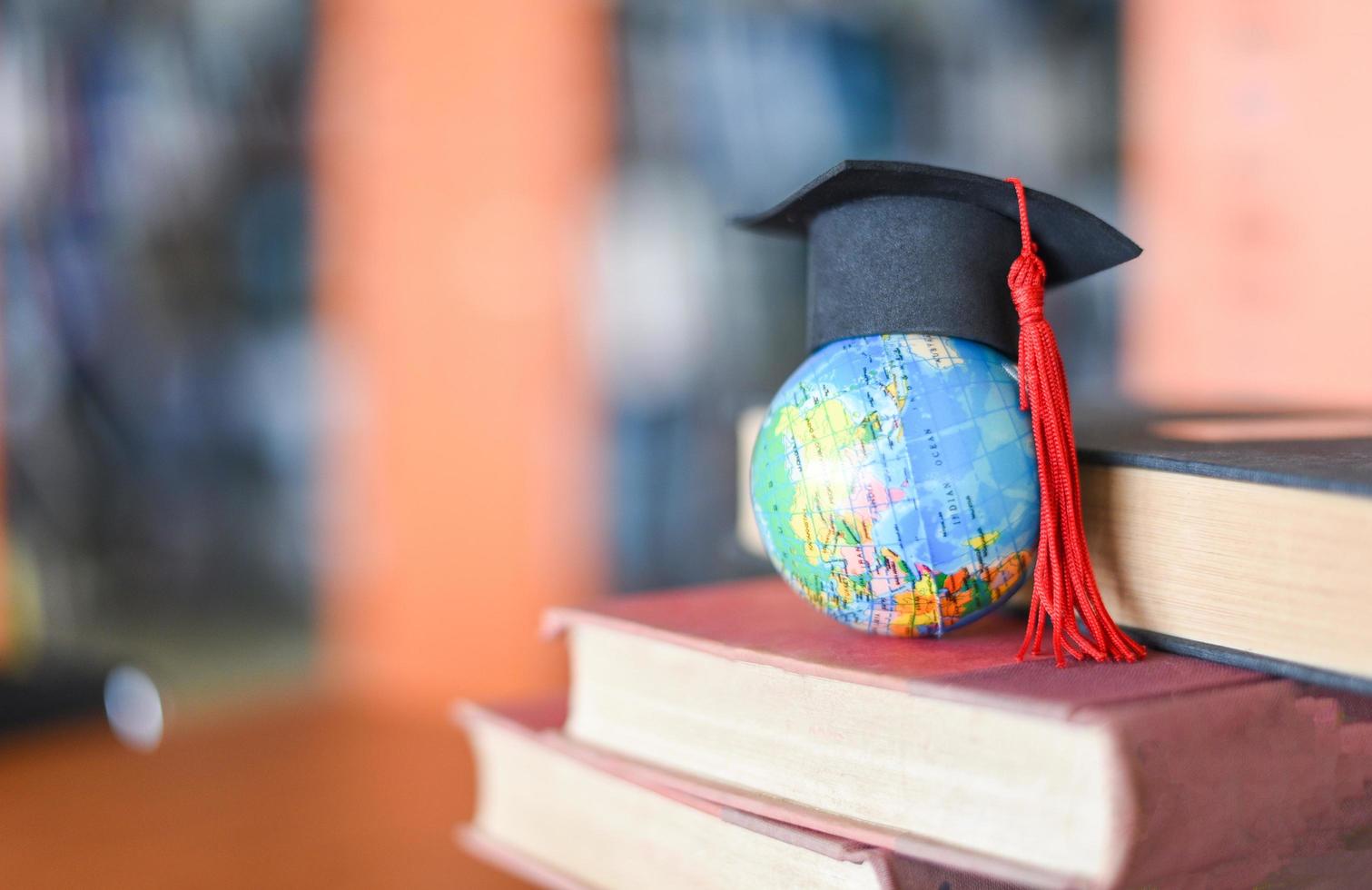 Books on the table in the library Education learning old book stack and graduation cap on earth globe model on wood desk and blurred bookshelf room background photo