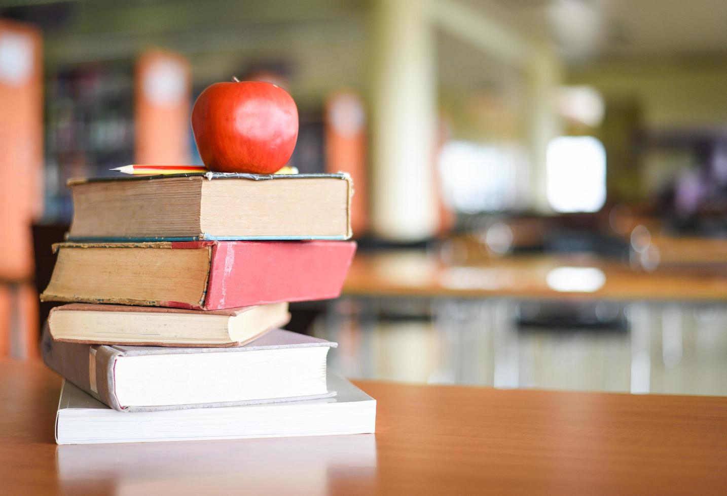 An apple on the books on the table with bookshelf in the library